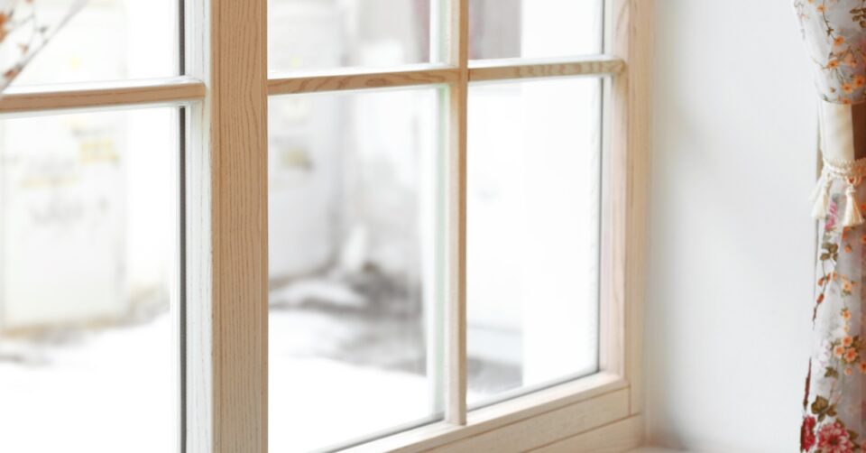 Sunlight shines through the glass of a large window with wooden frames, with floral print curtains adorning it.
