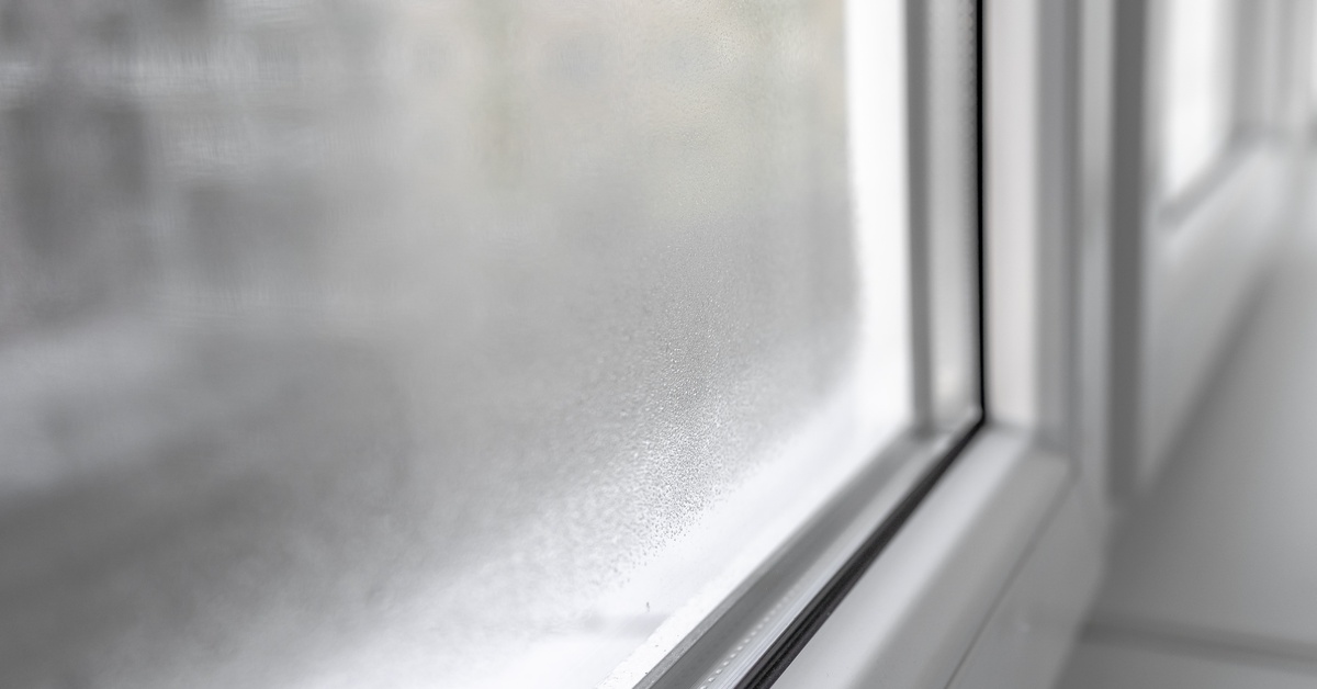 The build-up of water condensation on the surface of a window constructed of plastic, with a white frame.