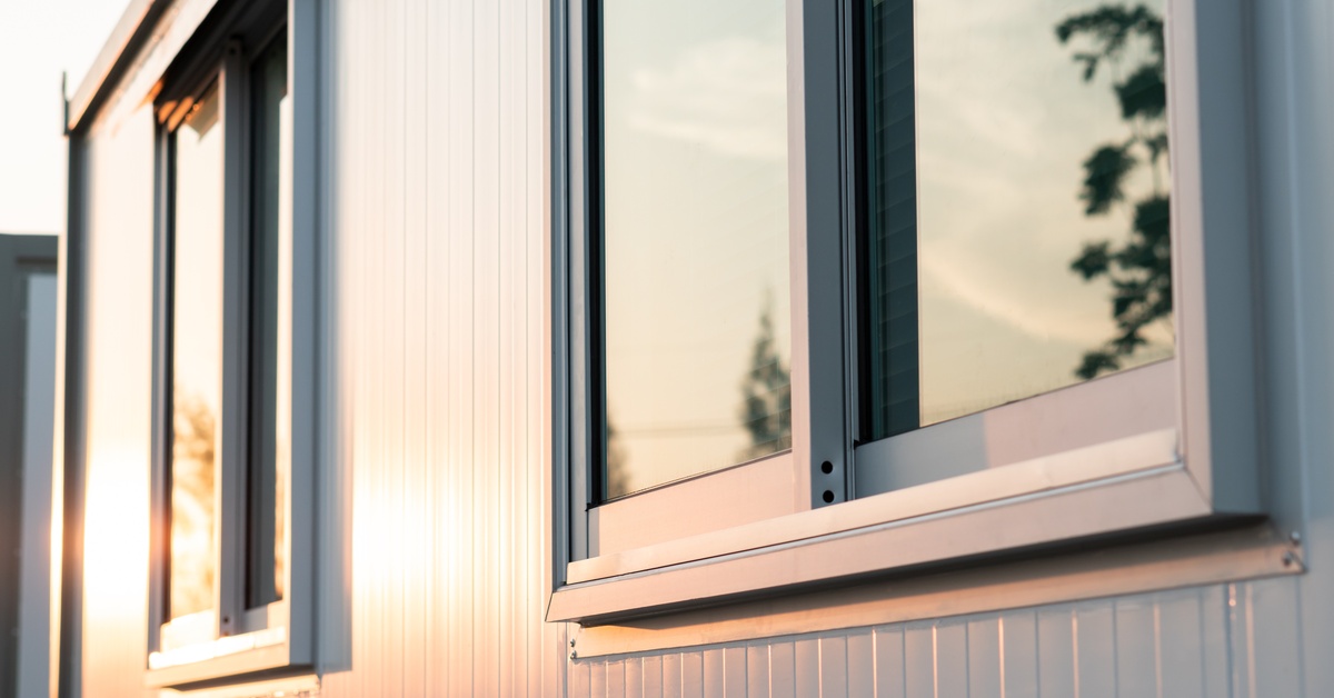 The reflection of sunlight and parts of trees on the surface of two windows on the exterior of a home.