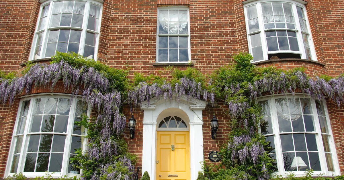 The brick façade of a large house with four bow windows. The windows have white drapes on them inside the house.