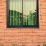 The brick exterior of a property that has green plants growing against it. The property has windows with black frames.