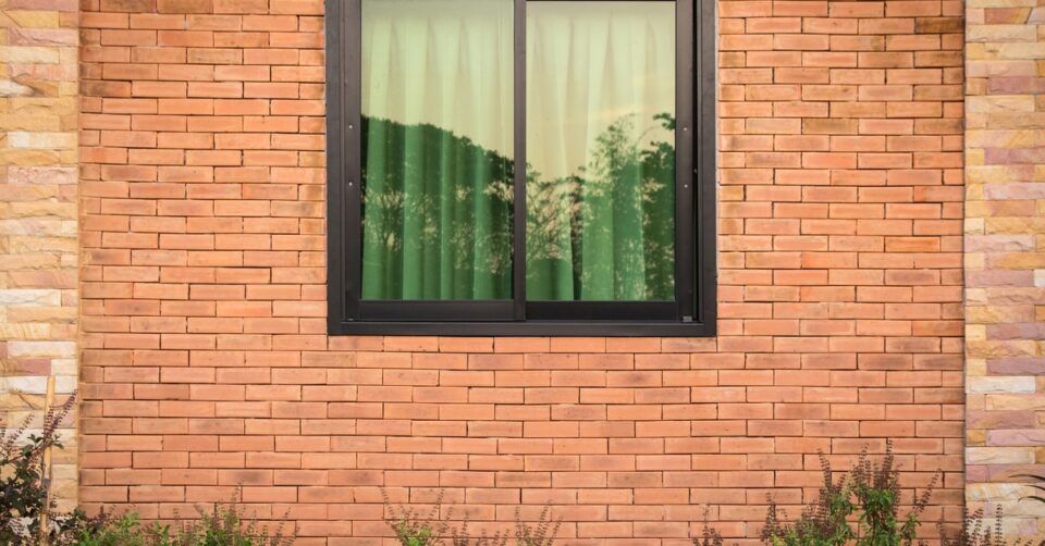 The brick exterior of a property that has green plants growing against it. The property has windows with black frames.
