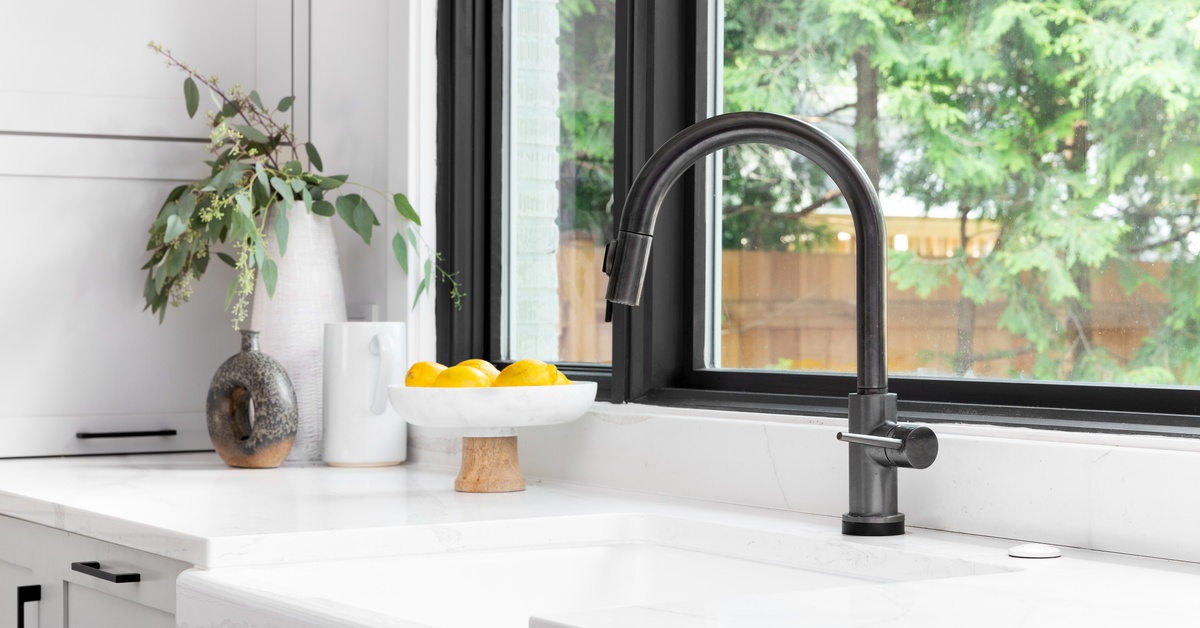 A kitchen with white walls and a window with a black frame that matches a black faucet installed on a white sink.