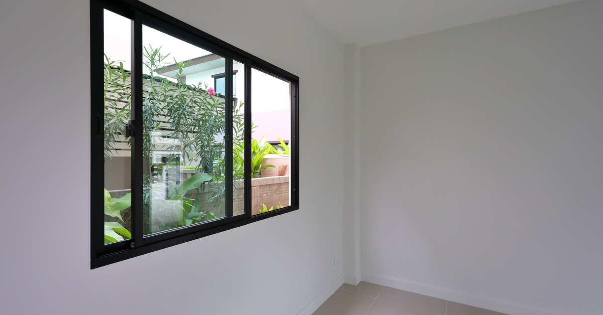 A window with a black frame installed in a room with white walls. The room does not have furniture in it.