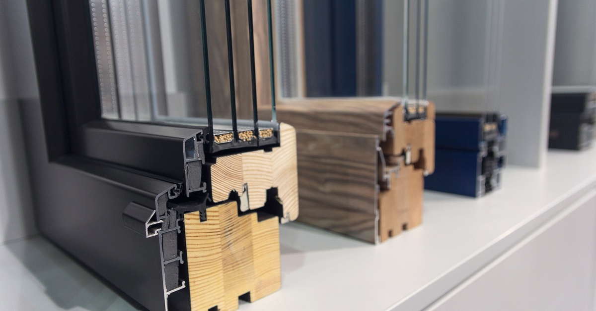 Several wooden and aluminum window profiles lined up neatly in a row on top of a plain white surface.