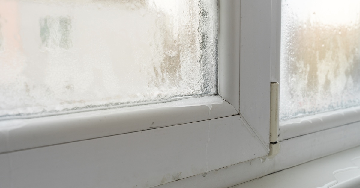 A close-up of a white window frame covered in a thin layer of melting ice. A puddle of water forms on the sill.
