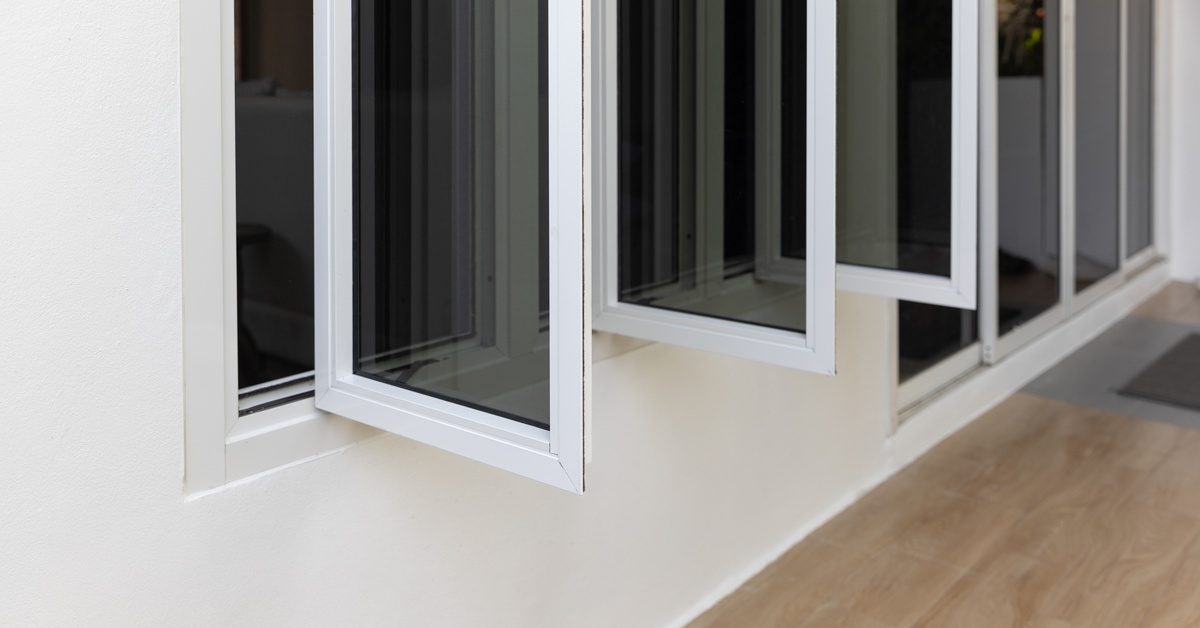 A casement window with three panels made of aluminum with white frames. There are hardwood floors below.