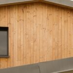 Part of a building with a brown metal roof, wooden siding, and a window with a black metal-clad frame.