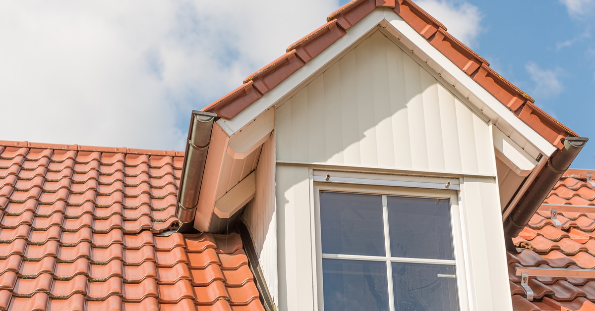 A close-up of a dormer window with a white metal-clad frame situated near the red tiled roof of a building.