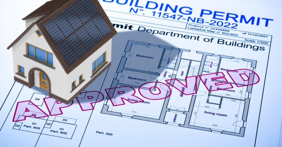 A model house sitting on top of a document entitled "Building Permit," with the word approved written across its cover.