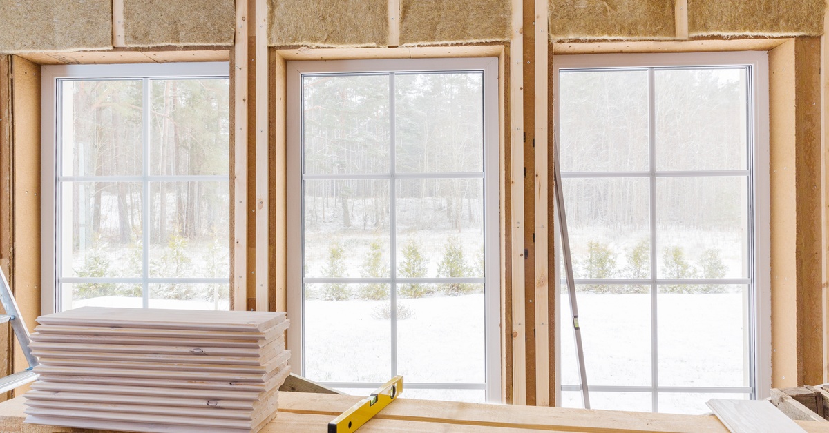 Large windows installed into a wall. A table with wooden boards and a laser line level on it sits in front of the windows.