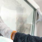 A close-up of a person wearing work gloves pressing against a white vinyl window frame during installation.
