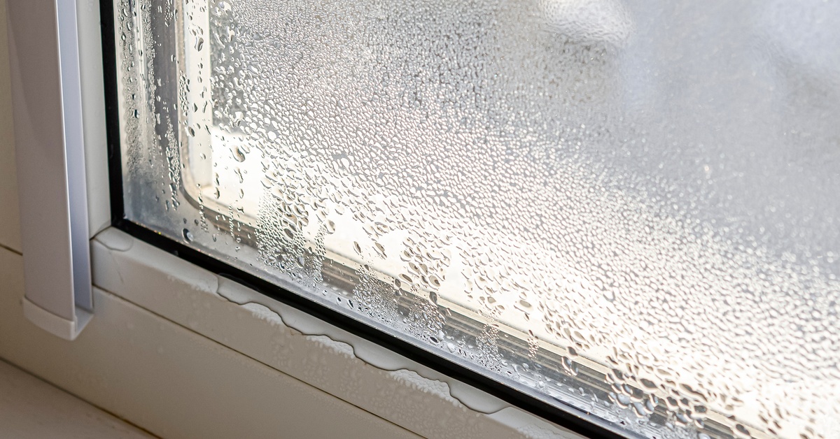 A close-up of the corner of a window. Condensation is built up on the glass, and water has seeped onto the windowsill.