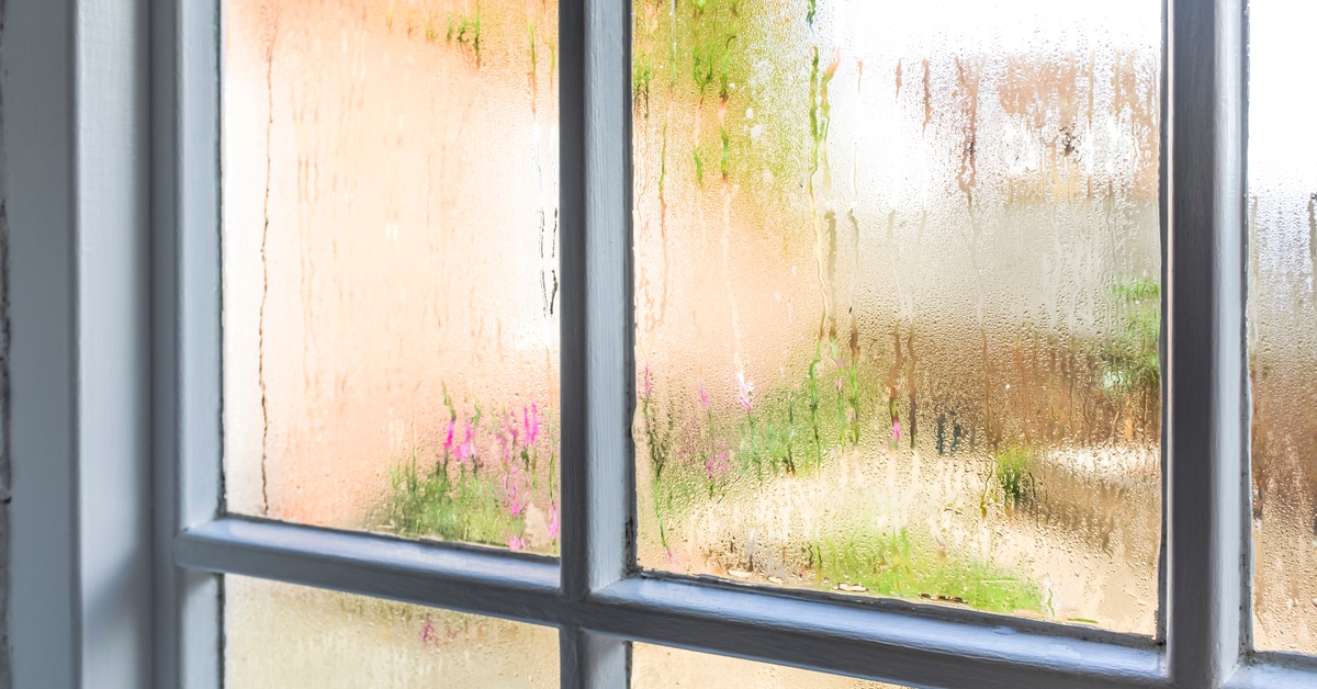 A white wood-paned sash window is fogged up. Streaks from water droplets run down the panes of glass.