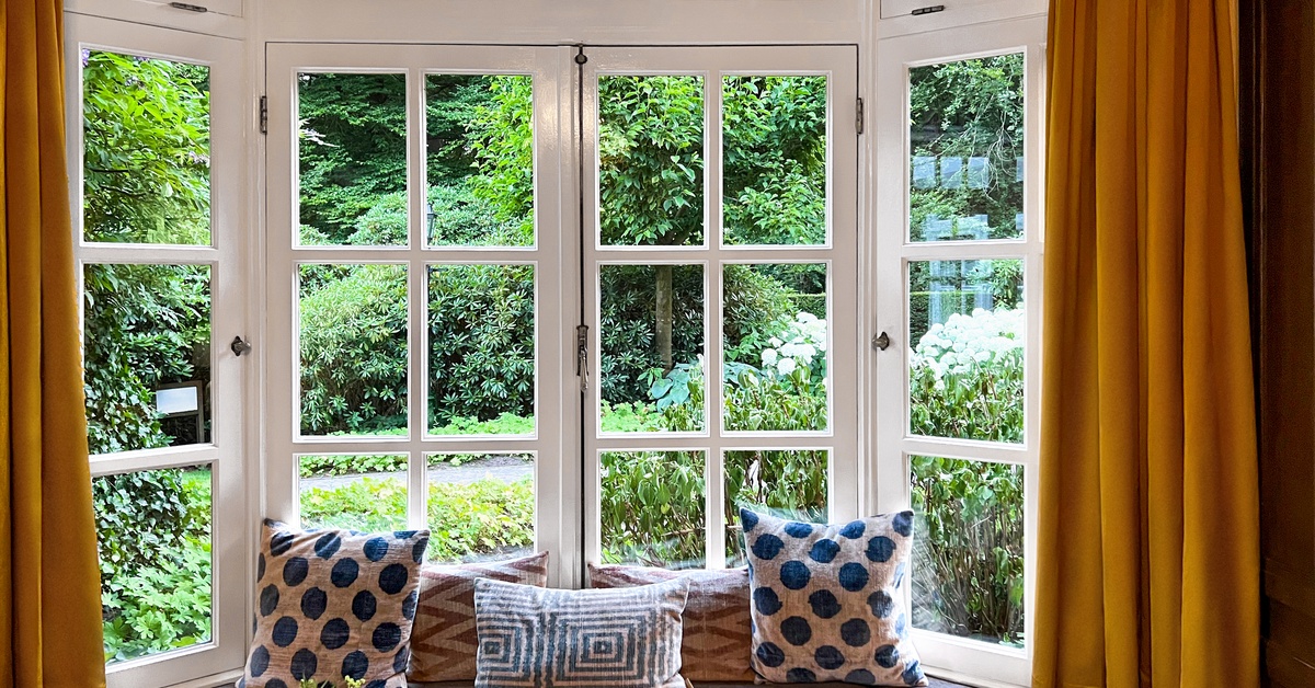 A set of bay windows with a built-in bench going around the bottom. Decorative pillows line the bench.