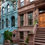 A row of historic brownstones lines a street. They're all different colors with uniquely shaped windows.