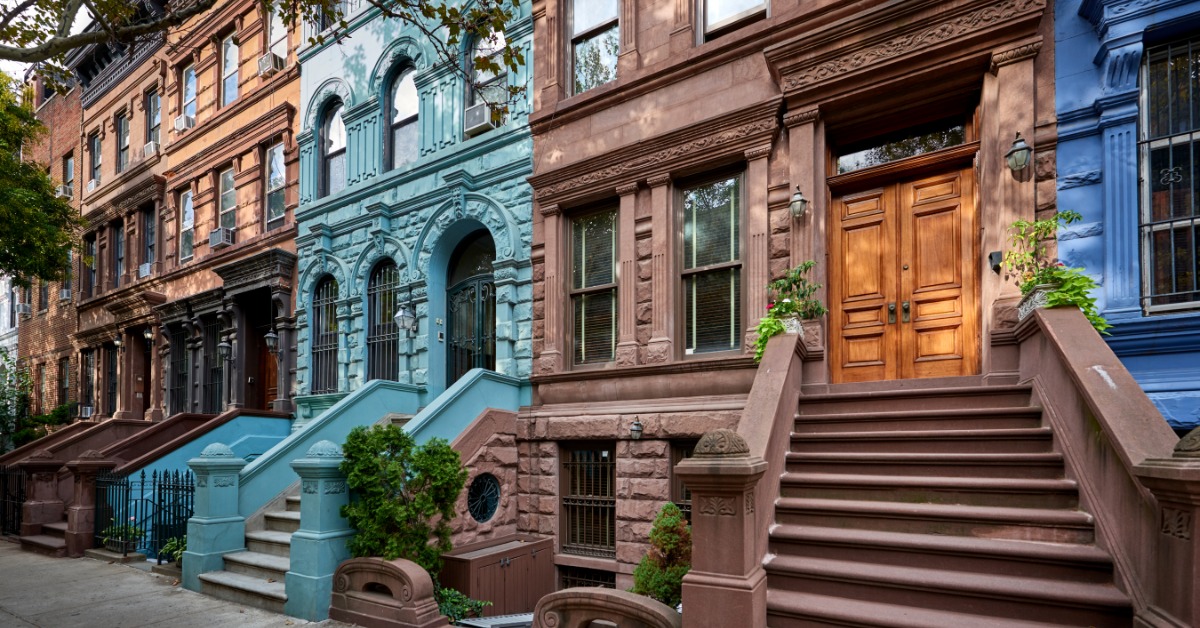 A row of historic brownstones lines a street. They're all different colors with uniquely shaped windows.