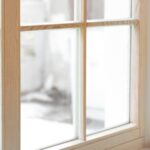 A set of large, wooden windows, seen from the inside of a home with curtains with warm floral patterns on either side.