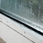 A close-up of the trim of a white window with heavy condensation on the window, dripping down to the trim.