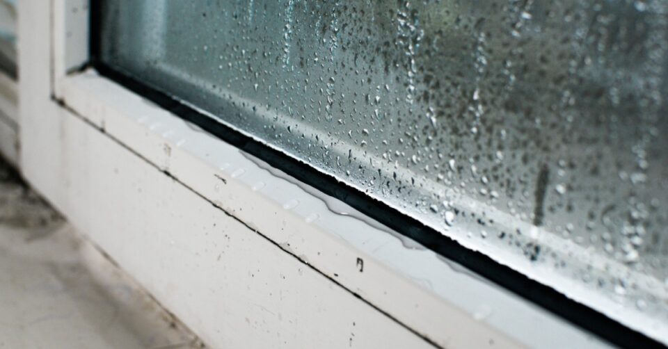 A close-up of the trim of a white window with heavy condensation on the window, dripping down to the trim.