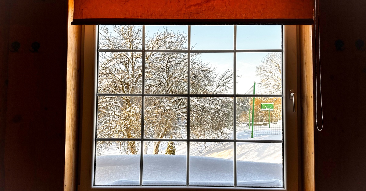 A rustic wooden window with snow outside, frosted glass, winter trees, and bright light coming through.