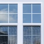 A white double-hung window with grilles set in horizontal vinyl siding on the exterior wall of a home.