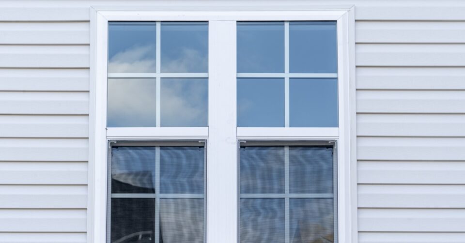 A white double-hung window with grilles set in horizontal vinyl siding on the exterior wall of a home.